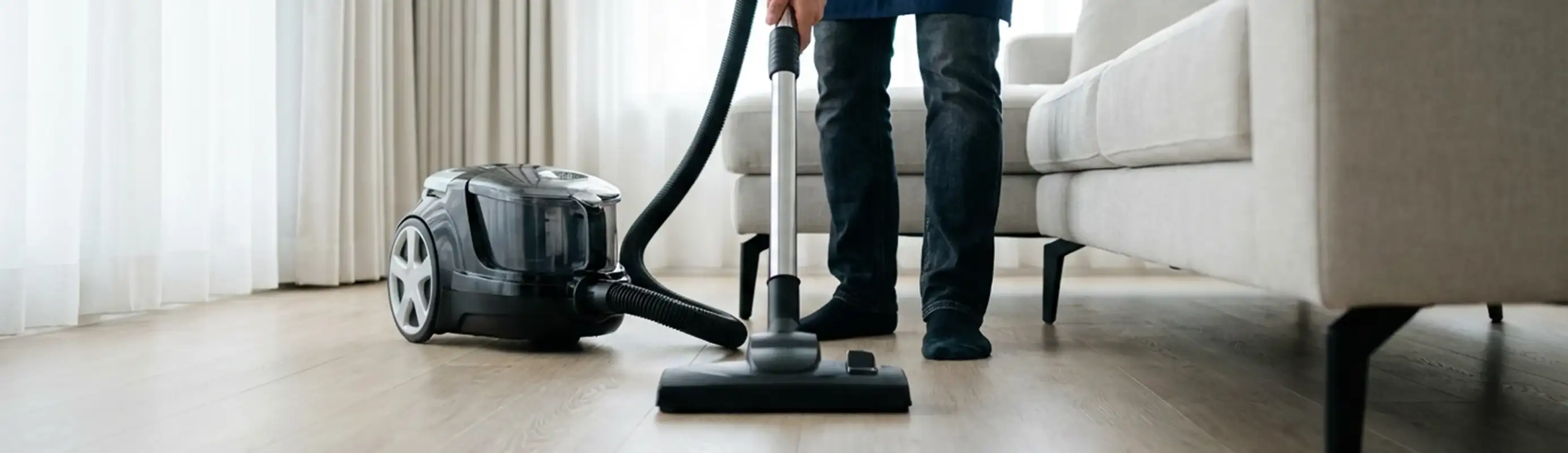 Professional house cleaner vacuuming a living room floor with a canister vacuum cleaner, Pueblo, CO.