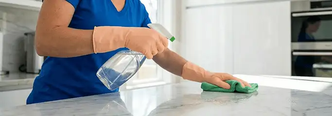 Maid service worker spraying and wiping a kitchen countertop with a microfiber cloth for sanitizing, Pueblo, CO.