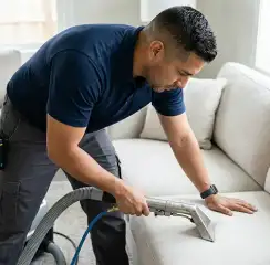 Professional upholstery cleaning technician using an extraction wand to deep-clean a fabric sofa, Pueblo, CO.