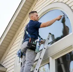 Professional window cleaner on a ladder using a squeegee to clean an exterior arched window, Pueblo, CO.