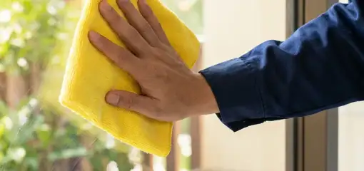House cleaner wiping a glass window with a yellow microfiber cloth for streak-free cleaning, Pueblo, CO.